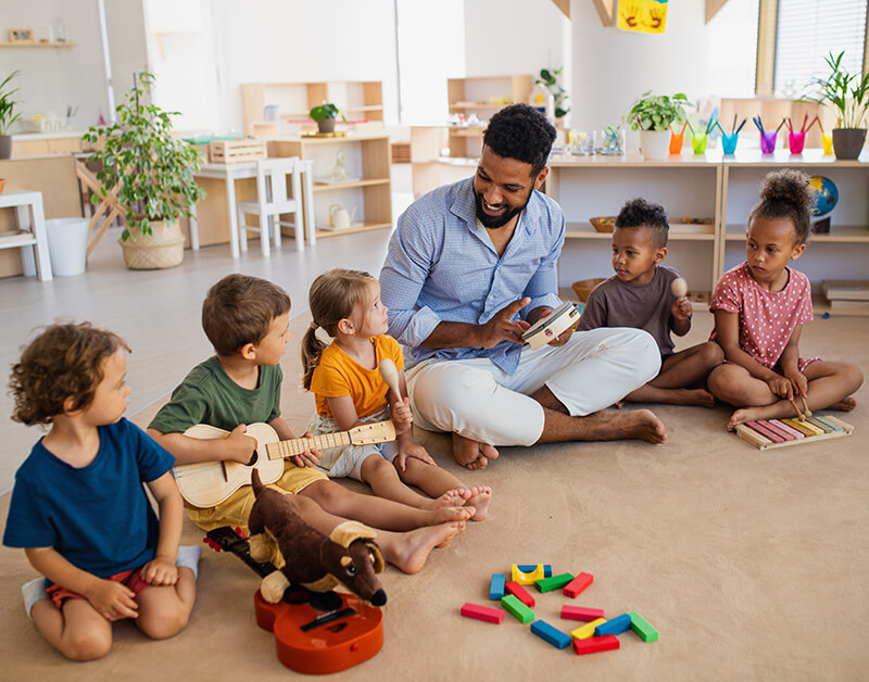 Group of children with their teacher siting on the floor playing instruments